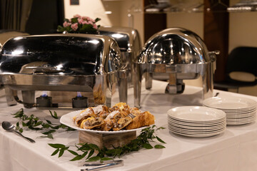 Breakfast bakery pastries on platter next to white plates and silver pots during catering event