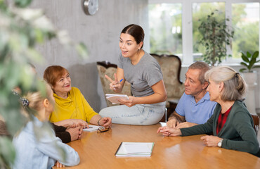 Young woman psychologist together with elderly adults have group therapy round table