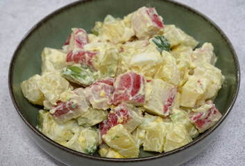 Seafood salad. Closeup view of a fresh salad with boiled sliced potatoes, chopped hard boiled egg, avocado, crab sticks and mayonnaise in a bowl on the white table