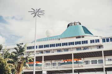 A close-up of a large modern cruise ship docked in port. Visible are several decks with windows,...
