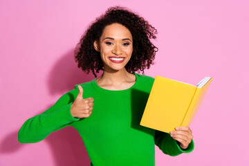 Photo portrait of attractive young woman hold read book thumb up dressed stylish green clothes isolated on pink color background