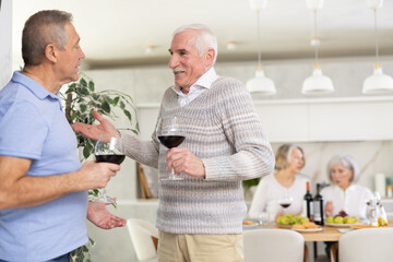 Elderly men drink red wine and tell each other news during a festive dinner at home
