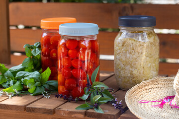 Fermentation of cherry tomatoes and cabbage on a wood garden cart with basil leaves and straw hat