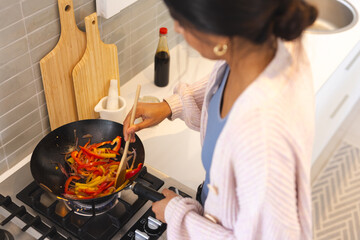 Asian woman cooking colorful vegetables in wok at home kitchen
