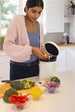Asian woman composting vegetable scraps in kitchen, promoting eco-friendly lifestyle, at home