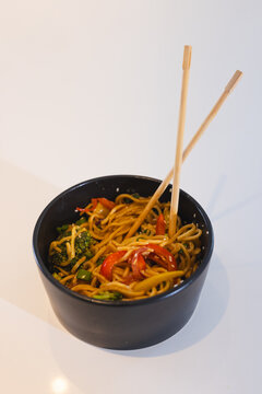 Delicious stir-fried noodles with vegetables in black bowl with chopsticks, at home