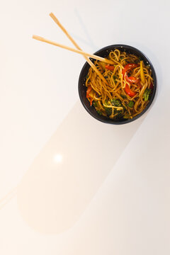 Chopsticks resting on bowl of colorful stir-fried noodles with vegetables, copy space, at home