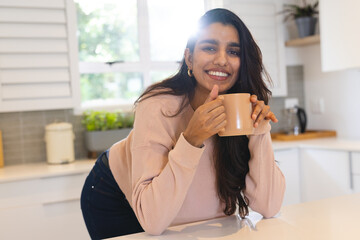 Smiling Asian woman enjoying coffee in bright kitchen, feeling relaxed and happy, at home