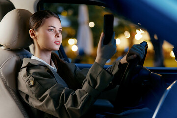 Woman driver looking at her phone a woman seated in a car's driver's seat, holding her cell phone,...