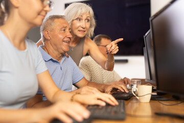 Smiling friendly older female mentor explaining something to motivated elderly man mastering...