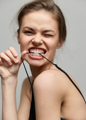 Joyful young woman playfully biting a strap, showcasing confidence and mischief. Light gray background enhances her fun and expressive emotions.