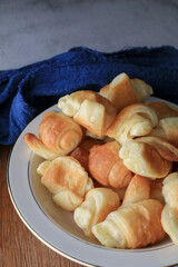 Mini croissant eat with coffee or tea in white pate on wooden board. French bakery, sweet dough dessert. Breakfast baked.