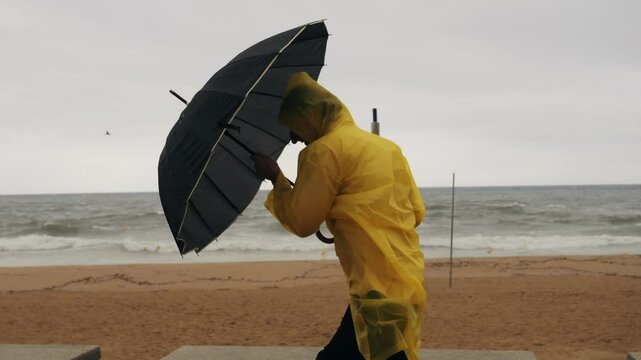 Man tourist person with umbrella and raincoat near sea ocean beach with storm on rainy european city street, lights reflecting, walking in Barcelona or Amsterdam during the rain.