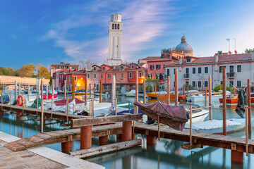 Morning view of calm canal in Venice with colorful buildings and boats moored along waterway, Italy