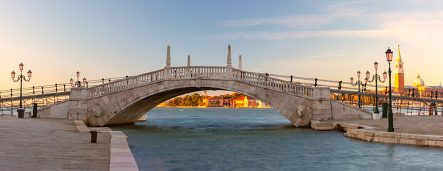 Panoramic view of stone pedestrian bridge and San Giorgio Maggiore illuminated by the rising sun, Venice, Italy