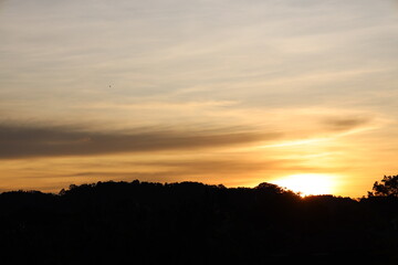 sunrise above rain forest covered hills paints high thin clouds pastel hues of pink orange gold...