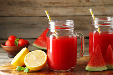 Tasty watermelon drink in mason jars and fresh fruits on wooden table, closeup
