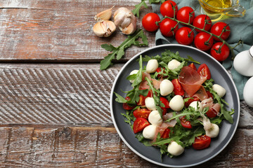 Tasty salad with arugula, mozzarella cheese, tomatoes and jamon on wooden table, flat lay. Space for text