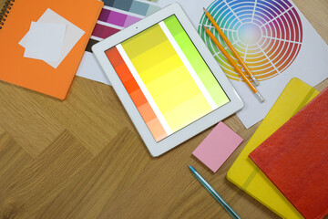 Designer's workplace with tablet, palettes and stationery on wooden table, flat lay