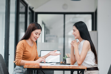 Fototapeta premium Two women discussing work at a modern office table, showcasing teamwork and collaboration in a professional environment.