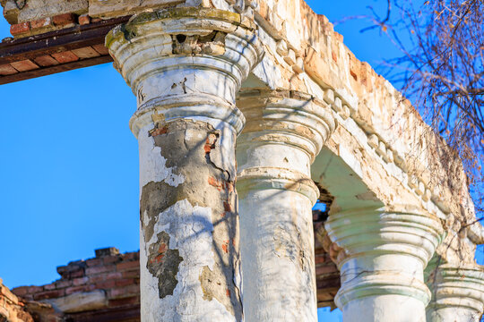 Old building columns with peeling plaster and cracks under blue sky, representing decay and classical architecture