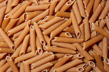 Uncooked Whole Grain Penne Rigate Pasta: A Culinary Canvas of Whole Wheat Macaroni, Creating a Lively and Textured Background for Gourmet Cooking. Whole Grain Dry Pasta. Whole Wheat Raw Macaroni