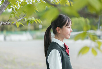 新緑の木の下にいる女性中学生の横顔