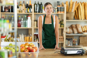Young female seller in apron posing at counter in grocery store