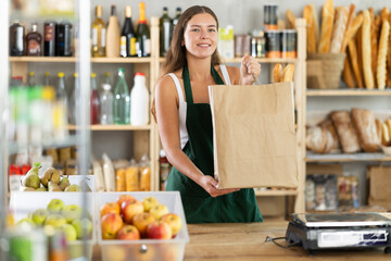 Portrait of positive girl supermarket seller with a paper bag of fresh products and a baguette