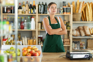 Young female seller in apron posing at counter in grocery store