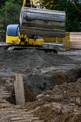 Construction excavator bucket scooping up gravel from a supply pile to dump into a dirt trench to...