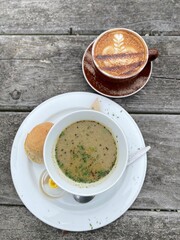 Cream of broccoli soup with bread on the white plate and a cup of coffee on the wooden table