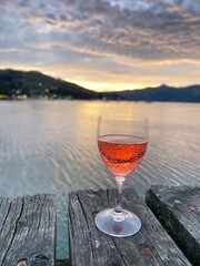 A glass of rose wine on the wooden table with beautiful lake views at the background 