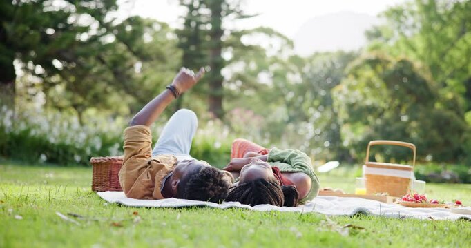 Black couple, relax and pointing for picnic on grass with romantic date, view and food basket of anniversary. People, direction and affection with loyalty, relationship bonding and commitment outdoor