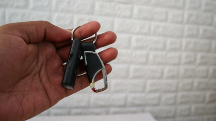 A close-up shot of a hand holding a keychain with a black leather strap and a metal carabiner clip,...