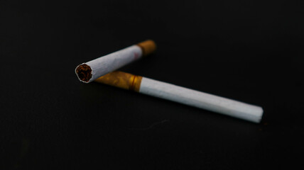Two cigarettes placed on a black surface, highlighting the contrast between the white paper and the dark background. Ideal for themes related to smoking, health, or lifestyle.
