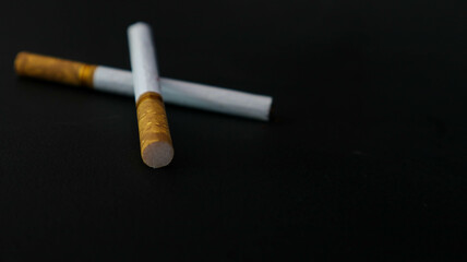 Two cigarettes placed on a black surface, highlighting the contrast between the white paper and the dark background. Ideal for themes related to smoking, health, or lifestyle.