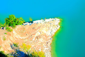 Captivating view at a white and reddish rock spike with sparse green trees descending into Lago di...