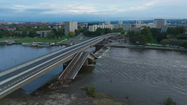 Aerial view of cars driving on a bridge over a river. Construction workers are repairing a section of the Carola bridge. The sun is setting in the distance
