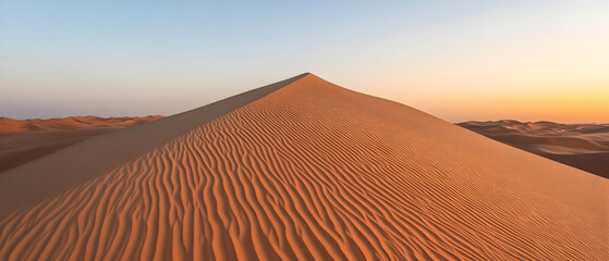 A lone sand dune in the desert, with the soft glow of the setting sun in the background.