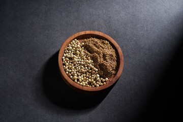 coriander seed and coriander powder in wooden bowl isolated on dark background, spice concept
