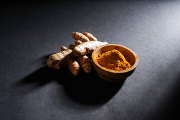 Fresh turmeric root and turmeric powder in a wooden bowl, turmeric isolated on dark background, spice concept