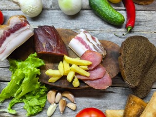 Dried meat and lard on a cutting board surrounded by vegetables.