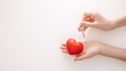 Two hands are positioned with a small key above a vibrant red heart, representing the idea of unlocking love and emotional security in a creative and artistic way.