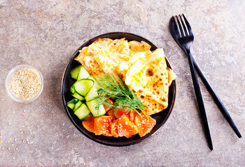 Thin pancakes or crepes with smoked salmon, cucumber and dill on a gray background.