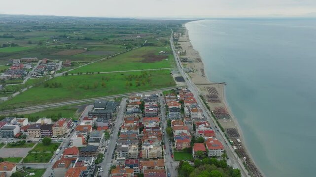 Aerial views showcase an empty beach, featuring nearby buildings, a winding road, the sparkling sea, and a vibrant green field, highlighting the stunning coastal and urban landscape
