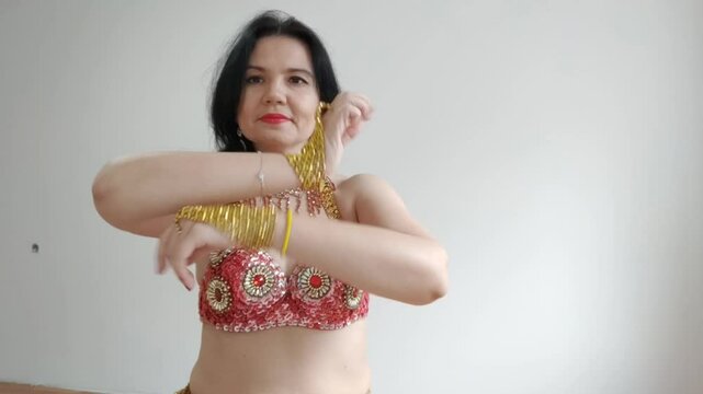 A dancer in a red suit is dancing an oriental dance on a white background. A professional dancer dances oriental belly dance. Sexy woman in red dress dances a seductive dance in a white studio