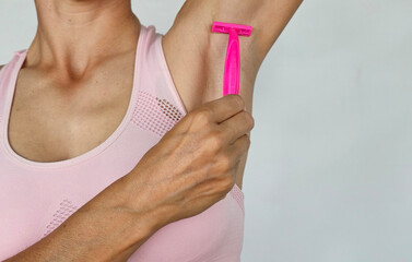 Woman shaving her armpits with a pink razor, focusing on personal grooming and hygiene