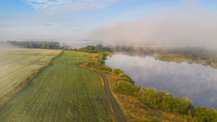 Dawn over the lake in the fog among the wheat fields