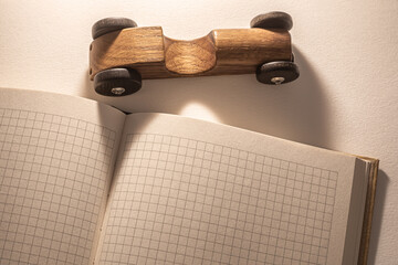 A wooden toy car rests atop an open notebook filled with grid paper, highlighting the planning...